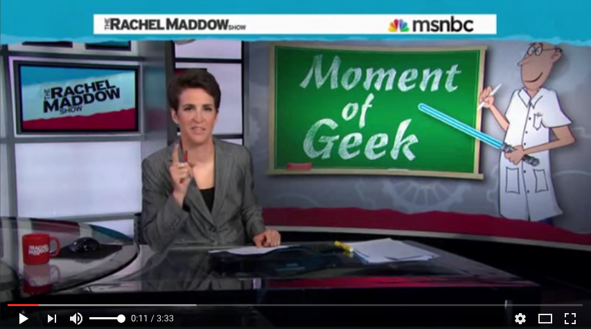 Rachel Maddow seated next to screen displaying text Moment of Geek