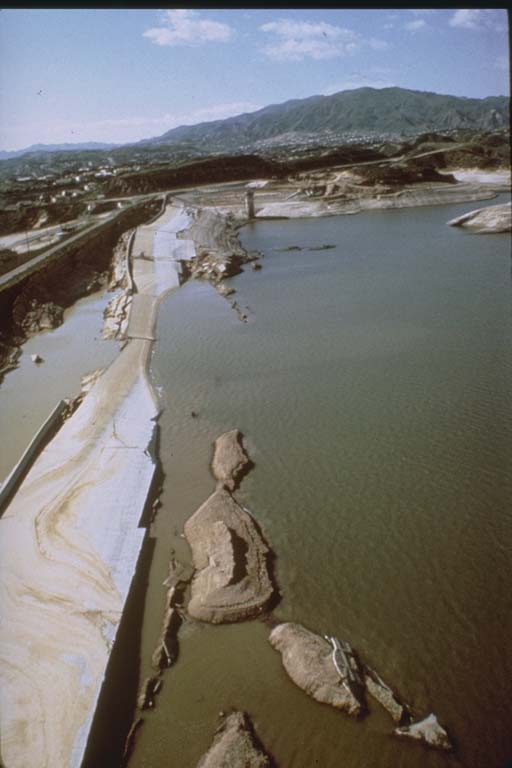 Old color photo of water nearly overtopping a crumbling dam.
