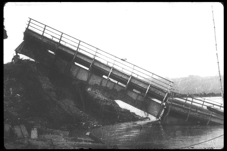Black and white photo of fallen bridge sitting in water.